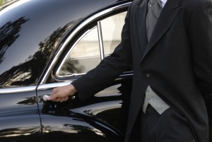 Close up photo of a chauffeur hand dressed with a frock coat, opening an antique cas«s door.